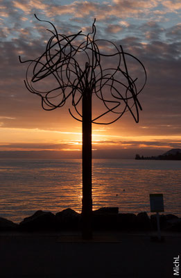 Sculpture monumentale en acier devant un lac au soleil couchant