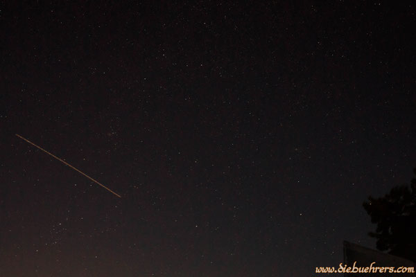 Blick in den Nachthimmel, links ein Flugzeug