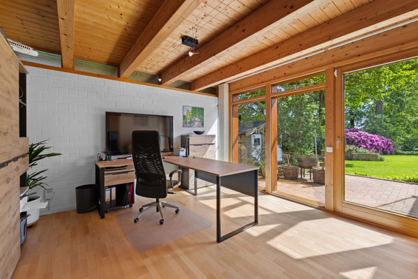 Arbeitszimmer mit Holzbalken an der Decke und großen Fenstern zur Terrasse 