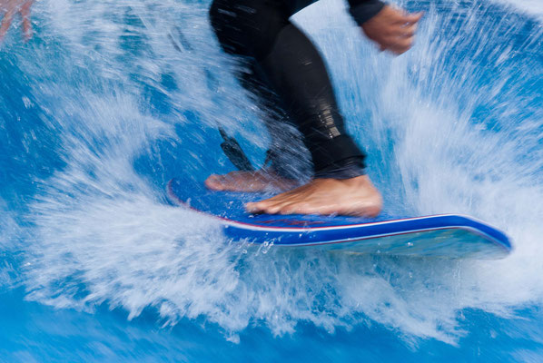 Nahaufnahme von Füssen auf einem Surfbrett in der Wellen beim Wellenreiten