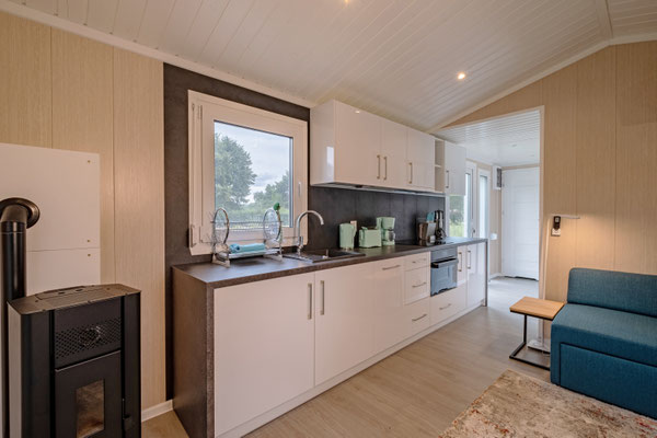 ein Tiny House mit heller Küchenzeile und Kamin, sowie Fenstern