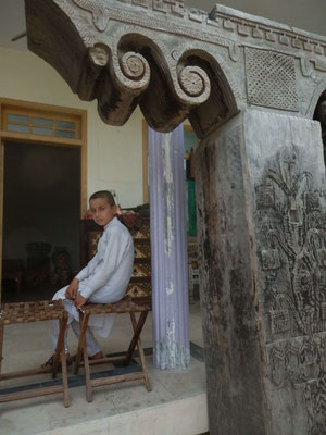A boy, maybe craftsman’s son, sitting behind an old pillar. 古い木柱の後ろに座る、職人の息子であろう少年。