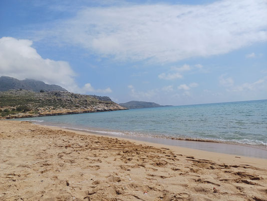 Im Vordergrund des Fotos ist der goldene Sandstrand zu sehen im Hintergrund erkennt man das blau gesprenkelte Meer und einen Abschnitt der grünen Küste.