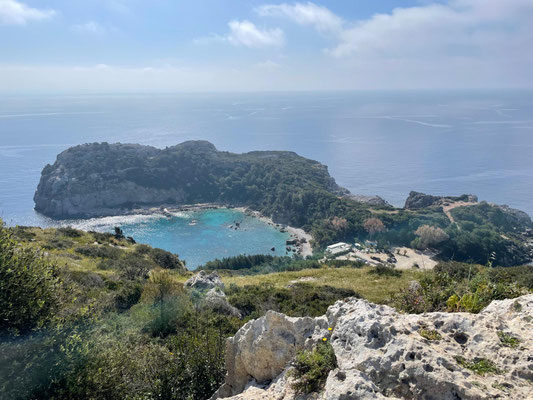 Das Foto zeigt den Ausblick auf die Anthony Quinn Bucht von weiter oben. In der Mitte des Fotos ist die blaue Bucht zu sehen, die von der grünen Küste der Insel umgeben ist.