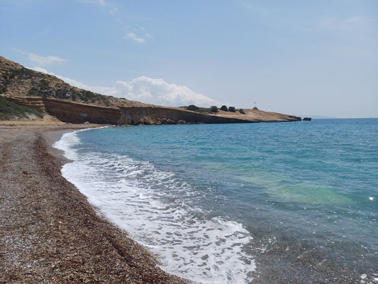 Das Foto zeigt einen Kiesstrand mit einem blauen Meer und niedrigen Wellen.