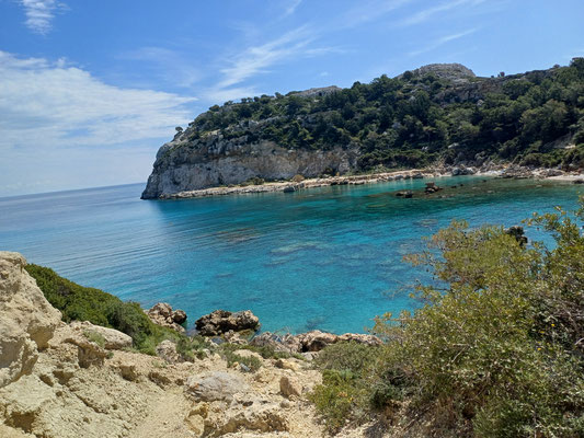 Das Foto zeigt den Blick auf die Anthony Quinn Bucht von oben. Neben dem K+stenabschnitt im Hintergrund ist das blau- und türkisgesprenkelte Meer zu sehen, welche sin verschiedenen Blautönen erstrahlt.