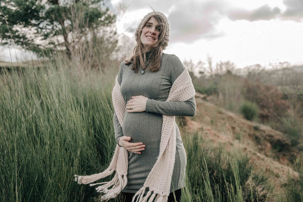 Szilvia Rölke Fotografie: Werdende Mutter umfasst lächeln ihren Babybauch bei einem Outdoorshooting.
