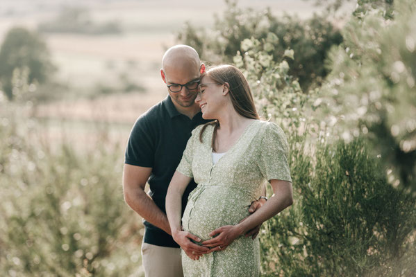 Schwangeres Paar schmiegt sich bei einem Outdoor-Babybauch-Shooting im Grünen in Ober-Mörlen aneinander.