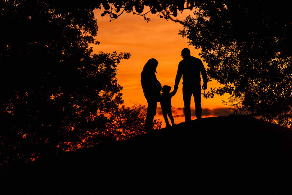 Familienfotoshooting im Herbst: Kind küsst den Babybauch der schwangeren Mutter.