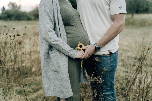 Nahaufnahme von Händen mit Sonnenblume am Babybauch, Outdoorshooting Bad Nauheim.