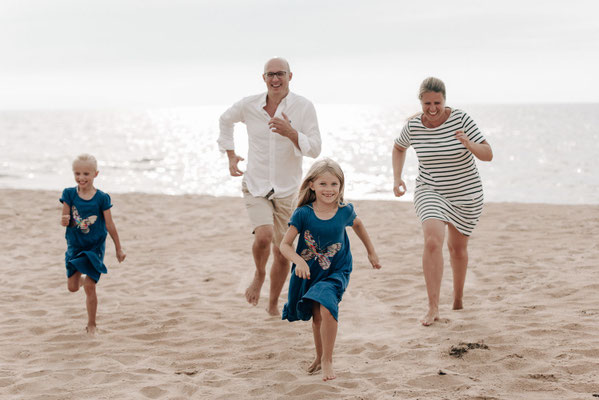 Eine vierköpfige Familie lacht und rennt barfuß am Sandstrand in Schweden.