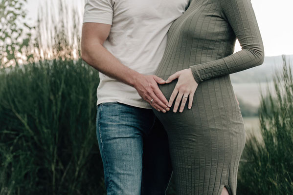 Detailaufnahme eines Babybauch-Shootings: Hände werdender Eltern formen ein Herz auf dem Bauch.