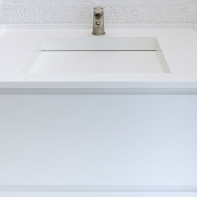 White solid surface vanity top with integrated sink where the drain is installed along one edge / fabricator: Gforma