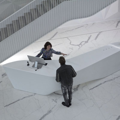 Large reception desk of unusual shape at a business centre fabricated from white solid surface