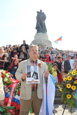 Ein Mann mit russischer Fahne und Foto eines Anhörigen vor dem Hügel mit dem Soldaten mit Kind auf dem Arm. Sowjetisches Ehrenmal Treptow. Foto: Helga Karl am 9. Mai 2015