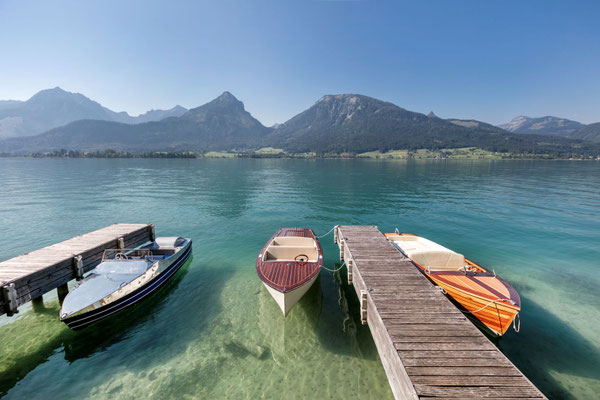 Holzsteg mit Booten am Wolfgangsee und türkisblauem Wasser im Salzkammergut
