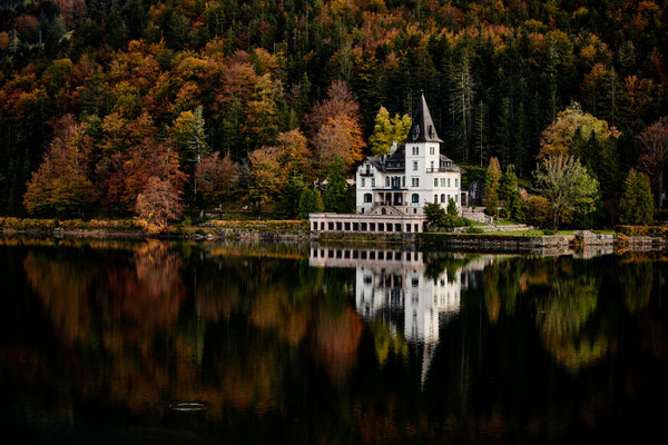 Schloss am Grundlsee mit herbstlicher Waldkulisse und Spiegelung im Wasser im Salzkammergut