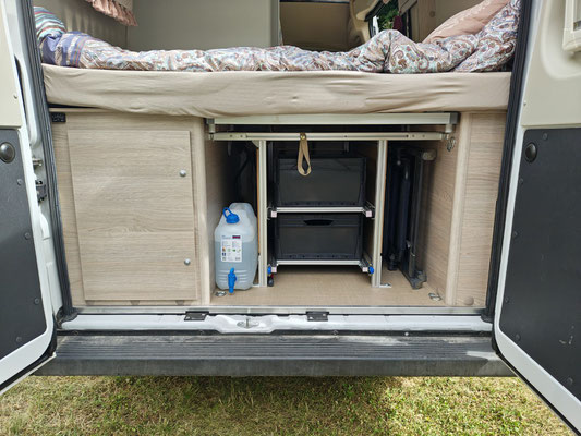 Hier der Endzustand: Links Tisch eingeschoben, davor Trinkwassertagesvorrat, mittig das Schubladensystem, rechts zwei Campingstühle und davor kommt der Fotorucksack.