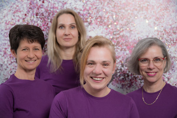 Vier Frauen, lächelnd mit violetten T-Shirts. Lächelnde Frau vor rosa Hintergrund mit violettem T-Shirt. Profesionelles Business Porträt.