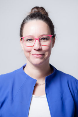 Frau mit rosaner Brille und blauem Blazer in Fotostudio vor grauem Hintergrund. Porträt von Sebastian Schieder, Fotograf Regensburg.