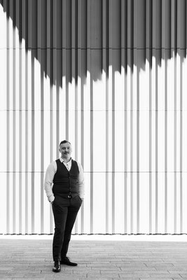 Künstlerisches Schwarzweiss Foto von Geschäftsmann mit Weste vor vertikal gestreiftem Hintergrund.