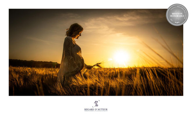 Une séance photo de grossesse réalisée en plein air au coucher du soleil, capturant la douceur de la maternité dans un champ.