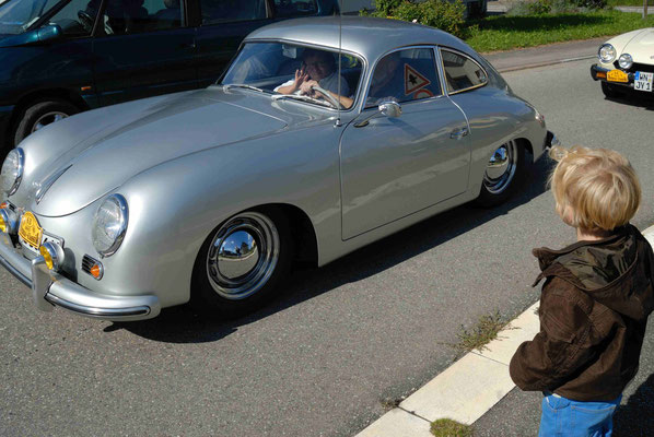 leiner Junge winkt Oldtimern bei einer Rallye vom Strassenrand zu