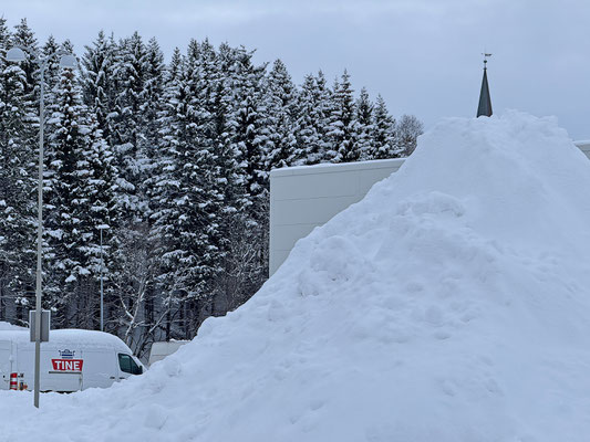 Dir Räumungsequippe häuft den Schnee vom Parkplatz bis zur Kirchturmspitze