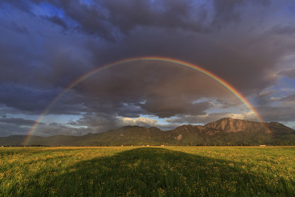 Regenbogen und Wolken vor Bergen