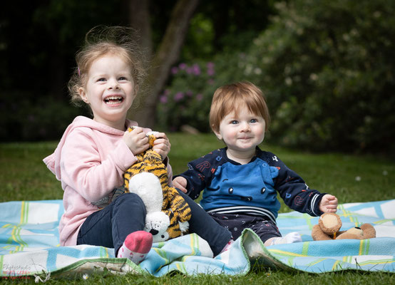 Das Bild zeigt ein Geschwisterpaar Kinder auf einer Picknickdecke beim Spaß haben.