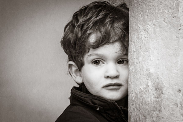 hier sehen Sie ein Portrait eines Jungen mit schwarzen Haaren angelehnt an eine Säule in schwarz weiß