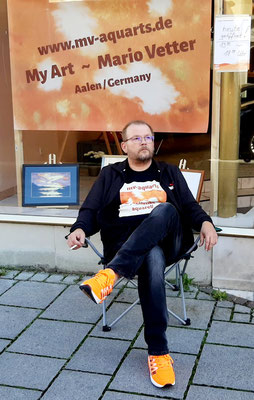 Der Künstler Mario Vetter sitzt gemütlich auf dem Stuhl vor dem Ladengeschäft, Ausstellung Ellwanger Herbst, Oktober 2023