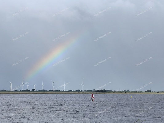 Ein Windsurfer am Meldorfer Mielespeicherbecken im bekannten Surfrevier "Speicherkoog Meldorf" vor einem Regenbogen
