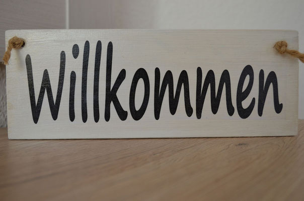 Schmales Holzbrettchen mit der Aufschrift ‚Willkommen‘ als herzlicher Gruß im Seitenelement der Haustür zur Ferienwohnung Olli.
