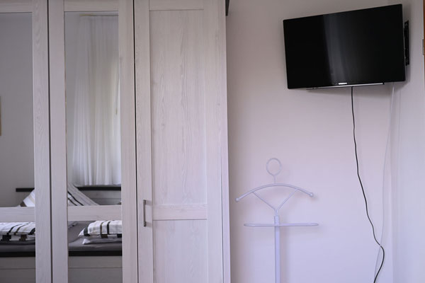 Ausstattung im Schlafzimmer der FeWo Olli mit TV-Gerät und geräumigem 5-türigem Spiegel-Kleiderschrank.
