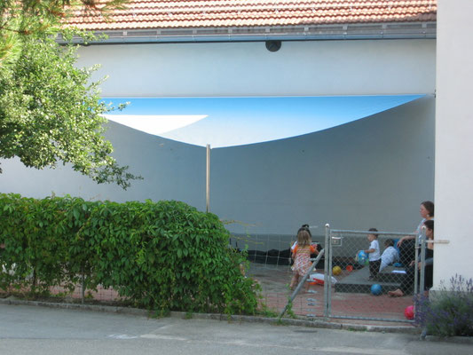 aufrollbares, dreieckiges Sonnensegel über einem Sandkasten eines Kindergartens