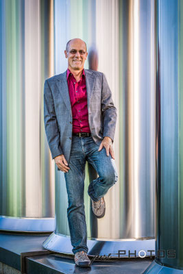 Mann in Jeans und mit Sakko lehnt lässig an silbernen Lüftungsrohren