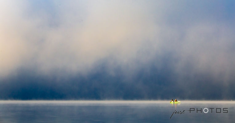 Dichter Nebel lichtet sich über dem Wörtsee, von der Sonne angestrahlt ein Fischerboot mit zwei Anglern