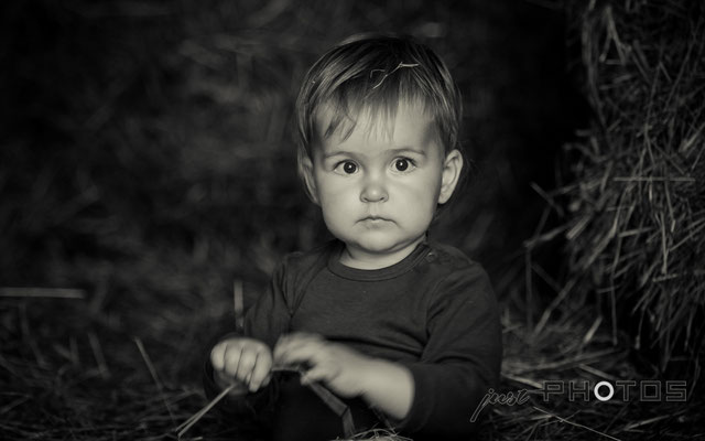 Kleines Kind sitzt im Heu (Stroh) und spielt an einem Halm