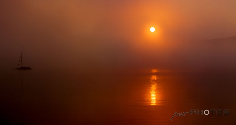 Sonnenaufgang am Wörthsee in extremem Orange, die Sonne spiegelt sich im dunklen Wasser