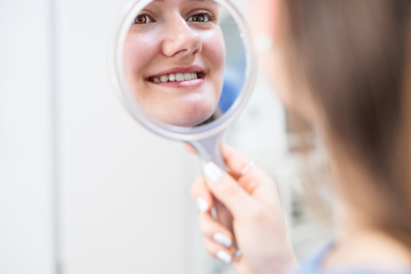 Zahnarztpraxis | Patientin betrachtet glitzernden Stein in ihrem Zahni m Spiegel 