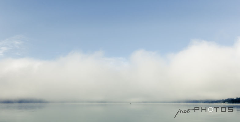 Nebelstimmung am Wörthsee, der Nebel steht wie Wolken über dem Wasser, in der Ferne ein Sportruderer