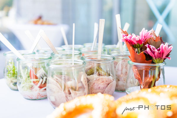 Finger-Food | Gläser mit Wurstsalat auf einem Bistro-Stehtisch | im Vordergrund Brezen und Blumen im Glas
