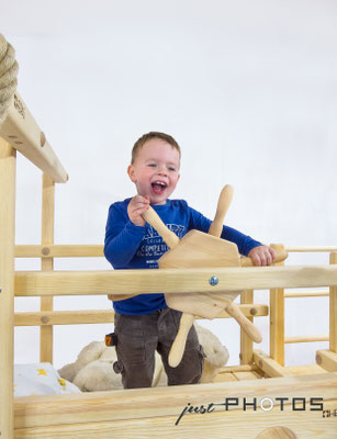 Junge steht in der oberen Etage an einem Spielbett (Abentheuerbett) und dreht mit Begeisterung an einem Holzlenkrad (Steuerrad)