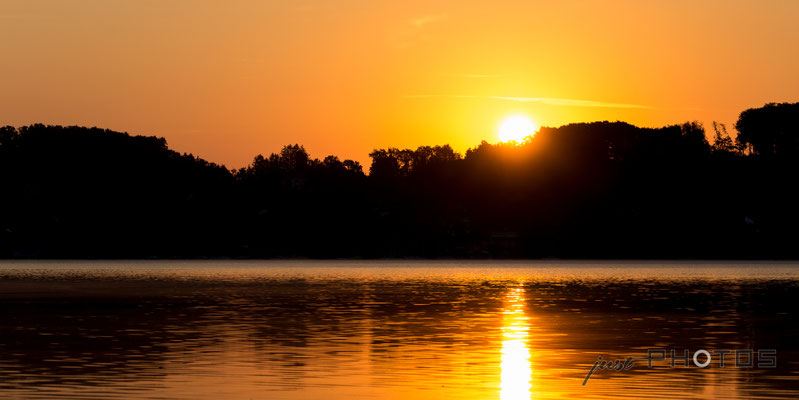 Sonnenaufgang am Wörthsee - die Sonne steigt hinter den Bäumen auf und spiegelt sich im Wasser