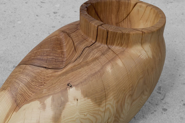 organic ash wood sculpture V1568 by Jörg Pietschmann. The smoothly carved piece evokes the intimate, protective curves of a woman's lap, featuring a prominent circular cavity at the top and flowing grain on a concrete floor.