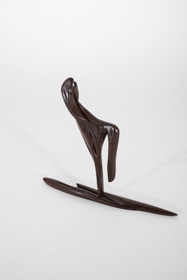 Abstract minimalist wood sculpture featuring a stylized, slender figure balanced on a horizontal needle-shaped base, crafted from dark brown polished hardwood with delicate organic grain details, isolated on a white studio background.