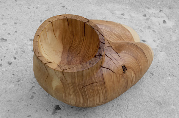 organic ash wood sculpture V1568 by Jörg Pietschmann. The smoothly carved piece evokes the intimate, protective curves of a woman's lap, featuring a prominent circular cavity at the top and flowing grain on a concrete floor.
