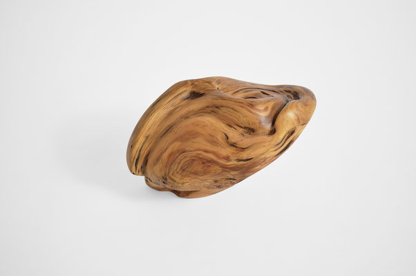 Abstract Aleppo pine wood sculpture S1369 by Jörg Pietschmann, showing a polished, golden-brown organic form with fluid, swirling grain patterns, wave-like dynamic lines, and dark natural accents on a solid white studio background.