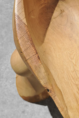 Organic oak wood bowl sculpture V1366 by Jörg Pietschmann, featuring a fluid, curved pedestal and a hollowed top, photographed outdoors against a weathered concrete wall.